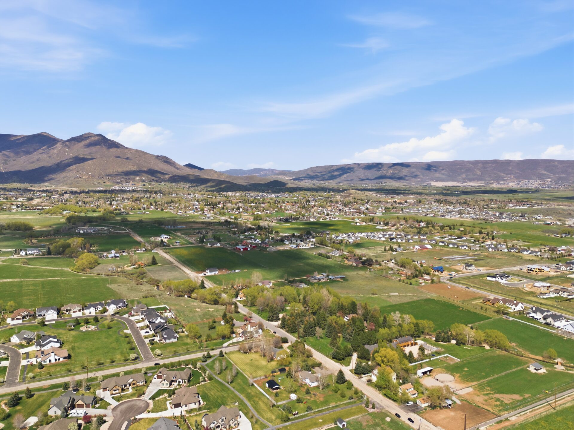 Aerial view of Midway Utah with green fields and snow-capped Wasatch Range mountains in the distance